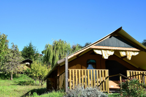 Safari tent called 'Tenda Luxury 2' in Italy, surrounded by greenery and clear blue sky.