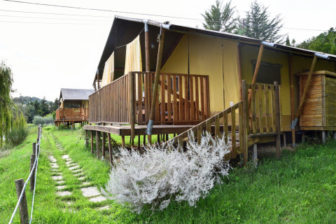 Tienda safari Tenda Luxury 3 en Italia, con terraza de madera y jardín verde en entorno natural.