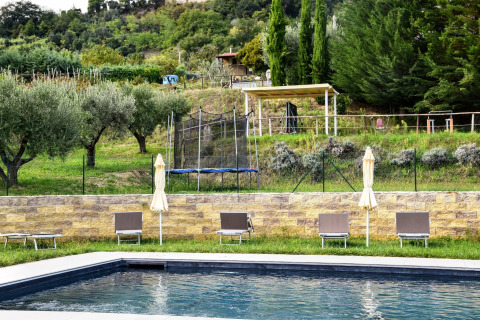 Piscina con tumbonas y sombrillas frente a colinas verdes en Tenda Luxury 3, Italia.