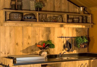 Zona cucina della tenda safari Tenda 1 in Italia con pareti in legno, mensole, piatti, erbe e utensili.