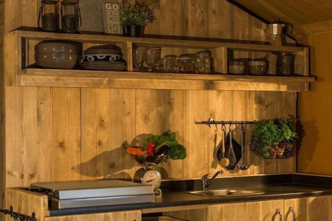 Keukengedeelte in safaritent Tenda 1 in Italië met houten wanden, planken, servies en kruiden.