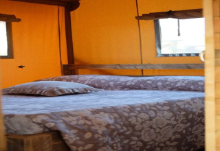 Binnenaanzicht van een tweepersoonsbed met bloemenbeddengoed in safaritent Tenda 1 in Italië.