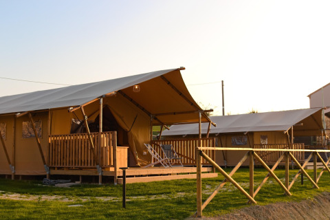 Safaritent Tenda 1 met houten veranda en hek, omgeven door gras, in het avondlicht.