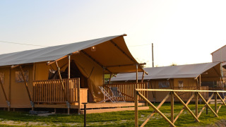 Tienda safari llamada Tenda 1, con terraza de madera y vallado, al atardecer soleado.