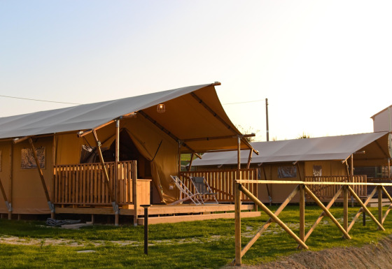 Safaritent Tenda 1 met houten veranda en hek, omgeven door gras, in het avondlicht.