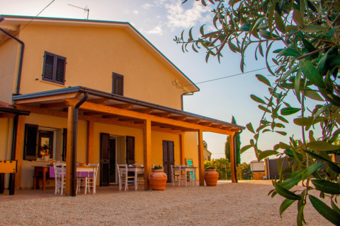 Buitenaanzicht van safaritent ‘Tenda 1’ in Italië met terras, tafels, stoelen en groene planten op de voorgrond.