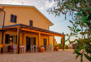 Buitenaanzicht van safaritent ‘Tenda 1’ in Italië met terras, tafels, stoelen en groene planten op de voorgrond.