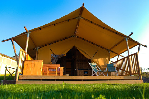 Safaritent 'Tenda 1' in Italië met houten veranda, stoelen en canvasdak onder een blauwe lucht.