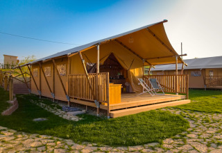 Tenda safari Tenda 1 in Italia con veranda coperta e sdraio su prato verde in una giornata di sole.