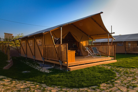 Safaritent Tenda 1 in Italië met overdekte veranda, ligstoelen en groene grasmat op zonnige dag.