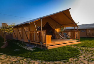 Safaritent Tenda 1 in Italië met overdekte veranda, ligstoelen en groene grasmat op zonnige dag.