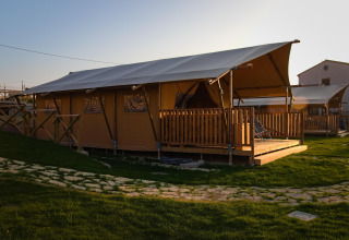 Safari tent 'Tenda 1' in Italië bij zonsondergang, met houten terras en groene grasvelden eromheen.