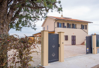 Ingang met zwart hekwerk, boom en villa bij Tenda 1, een safaritentaccommodatie in Italië.