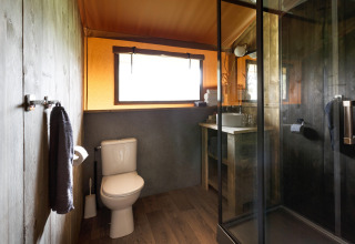 Moderne badkamer met douche, toilet en wastafel in een safaritentaccommodatie in Italië.