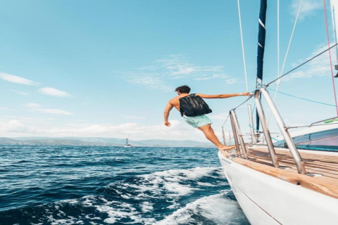 Een man met rugzak staat op de rand van een zeilboot en kijkt naar zee bij Tenda 1 in Italië.