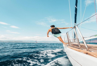 Een man met rugzak staat op de rand van een zeilboot en kijkt naar zee bij Tenda 1 in Italië.