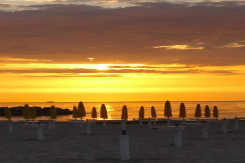 Zonsondergang op het strand vanaf safaritent Tenda 1 in Italië met gesloten gele parasols bij de zee.