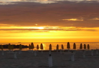 Zonsondergang op het strand vanaf safaritent Tenda 1 in Italië met gesloten gele parasols bij de zee.