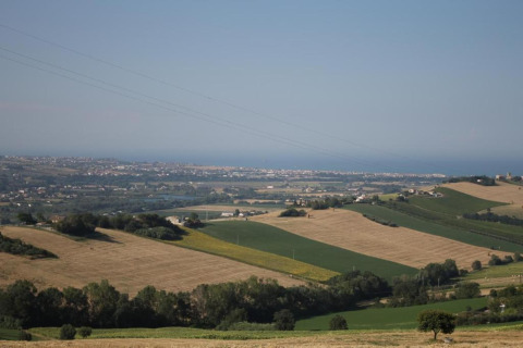Uitzicht vanaf safaritent 'Tenda 1' in Italië over glooiende velden, bomen en een stad aan de horizon.