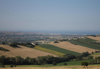 Uitzicht vanaf safaritent 'Tenda 1' in Italië over glooiende velden, bomen en een stad aan de horizon.