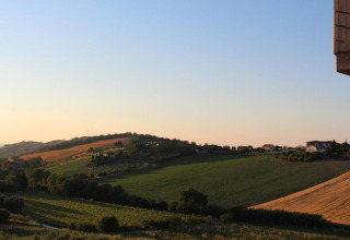 Uitzicht vanaf safaritent 'Tenda 1' in Italië over glooiende groene velden en heuvels bij zonsondergang.