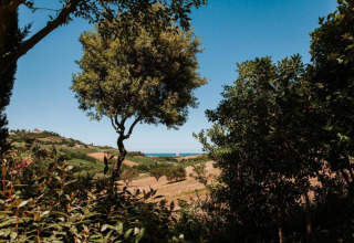 Uitzicht vanuit safaritent 'Tenda 1' in Italië op groene natuur, velden en de zee in de verte.