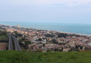 Uitzicht vanaf safaritent Tenda 1 in Italië op een kustplaats, snelweg, gebouwen en zee.