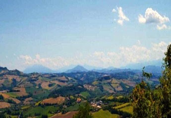 Uitzicht vanaf safaritent Tenda 1 in Italië op groene heuvels, velden en een heldere blauwe lucht.