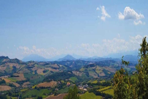 Uitzicht vanaf safaritent Tenda 1 in Italië op groene heuvels, velden en een heldere blauwe lucht.