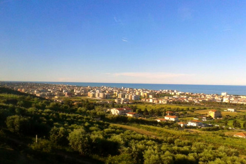 Vista dalla tenda safari Tenda 1 in Italia con campi verdi, la città e il mare sotto un cielo azzurro.