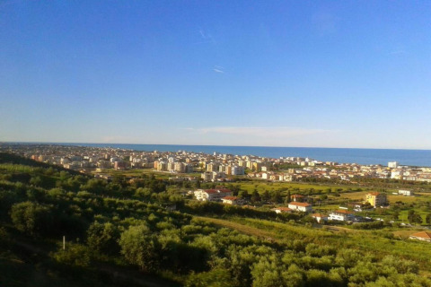 Uitzicht vanuit safaritent Tenda 1 in Italië met groene velden, stadsgezicht en de zee onder blauwe lucht.