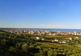 Uitzicht vanuit safaritent Tenda 1 in Italië met groene velden, stadsgezicht en de zee onder blauwe lucht.