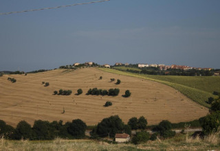 Uitzicht vanaf safaritent 'Tenda 1' in Italië met glooiende velden, bomen en een dorp op een heuvel.