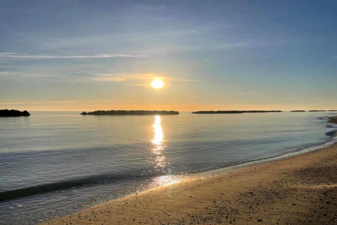 Alba su acqua calma e spiaggia sabbiosa, vista dalla tenda safari Tenda 1 in Italia con piccoli isolotti.