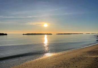Zonsopgang boven rustig water en strand, gezien vanaf safaritent Tenda 1 in Italië, met kleine eilandjes.