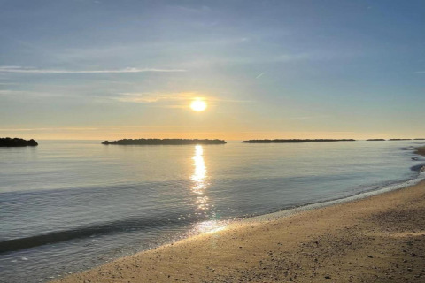 Zonsopgang boven rustig water en strand, gezien vanaf safaritent Tenda 1 in Italië, met kleine eilandjes.