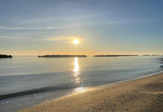 Zonsopgang boven rustig water en strand, gezien vanaf safaritent Tenda 1 in Italië, met kleine eilandjes.