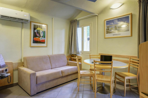 Mobile home living area with beige sofa, round dining table, wooden chairs, wall art, and air conditioning.