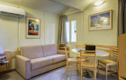 Mobile home living area with beige sofa, round dining table, wooden chairs, wall art, and air conditioning.