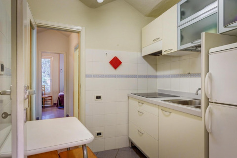 Helles Mobilheim-Küche mit weißen Schränken, Doppelkühlschrank, kleinem Tisch und Blick ins Schlafzimmer.