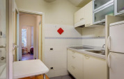 Bright mobile home kitchen with white cabinets, electric stove, fridge, small table and open bedroom view.