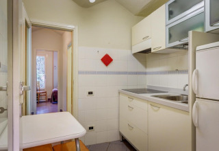 Helles Mobilheim-Küche mit weißen Schränken, Doppelkühlschrank, kleinem Tisch und Blick ins Schlafzimmer.