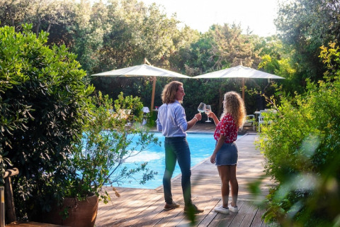 Two people clinking wine glasses by a pool at a mobile home, surrounded by lush green foliage