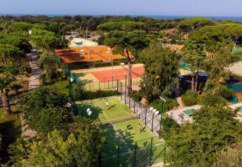 Aerial view of Holiday Resort Riva degli Etruschi in Italy, featuring tennis courts, trees, and the sea beyond.