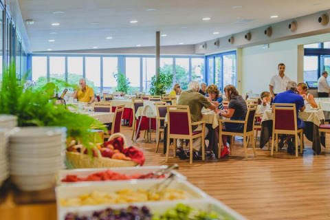 Dining area in a mobile home with guests eating at tables and a buffet of food visible in the foreground.
