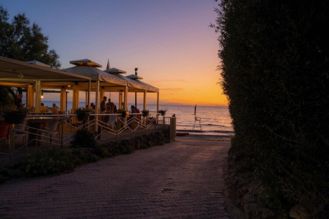 Sunset view by the sea with people dining under a pavilion near a mobile home park beachfront area.