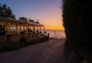 Sonnenuntergang am Meer mit Menschen, die ein Abendessen im Pavillon nahe einem Mobilheim genießen.