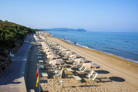 Beach lined with umbrellas and lounge chairs next to a walkway, overlooking the calm blue sea.