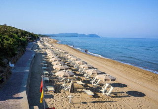 Strand mit vielen Sonnenschirmen und Liegestühlen entlang eines Weges mit Blick auf das ruhige Meer.