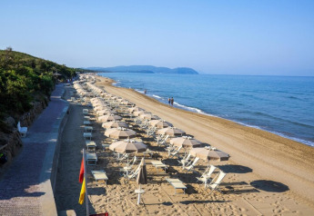 Beach lined with umbrellas and lounge chairs next to a walkway, overlooking the calm blue sea.